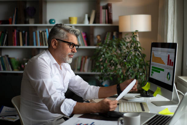 Man using desktop pc at desk in home office Man using desktop pc at desk in home office market research stock pictures, royalty-free photos & images