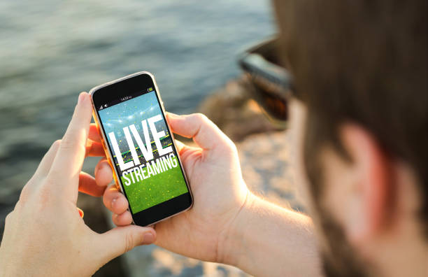 Man using his mobile phone on the coast live streaming man on the coast using his smartphone wih live streaming sports event. All screen graphics are made up. streaming service stock pictures, royalty-free photos & images