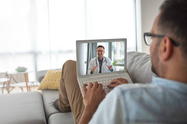 Man using laptop and having video call with his doctor Patient doctor online consultation. Back view of young man making video call with her doctor while staying at home. Man using laptop and having video call with his doctor telemedicine stock pictures, royalty-free photos & images
