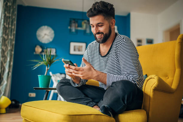 Man using phone Man sitting home in his armchair and using phone armchair photos stock pictures, royalty-free photos & images