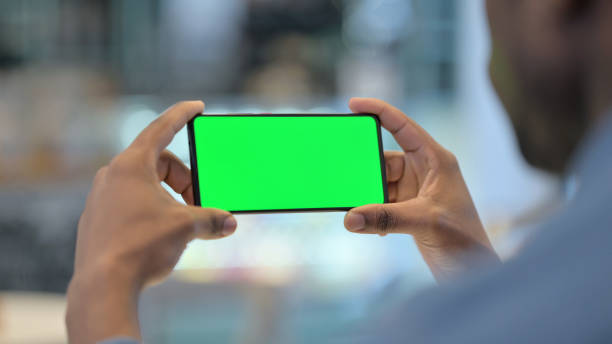 녹색 크로마 키 스크린, 리어 뷰와 스마트 폰을 사용하는 남자 - 수평 구성 뉴스 사진 이미지
