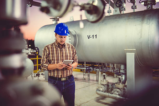Man using tablet at Natural gas processing facility Man wearing blue hardhat using tablet at Natural gas processing facility oil refinery stock pictures, royalty-free photos & images