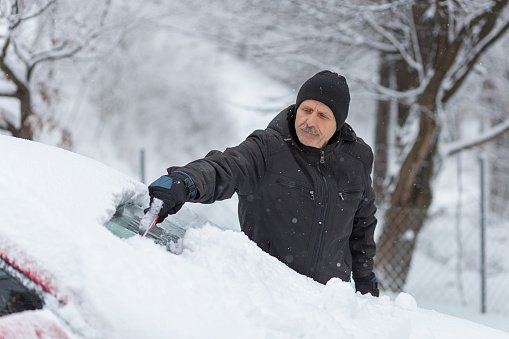 Older man holding ice scraper and removing snow from his car
