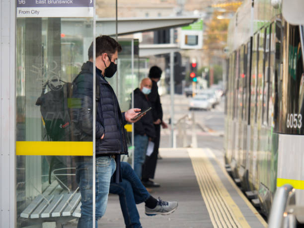 A man waits to get on at tram stop in Melbourne wearing mask stock photo