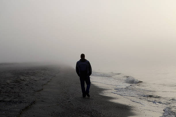 man walking alone on a foggy beach - bir erkek sadece stok fotoğraflar ve resimler