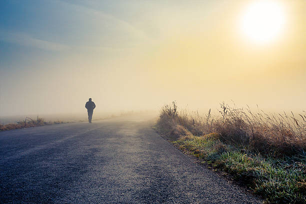 A man walking down a country road on a foggy morning stock photo