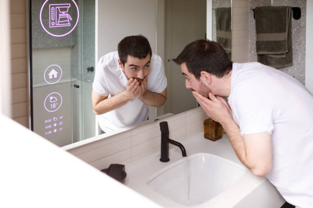un homme se lave le visage le matin pendant que le miroir de la salle de bain montre que le café est en cours de préparation - miroir connecté  photos et images de collection