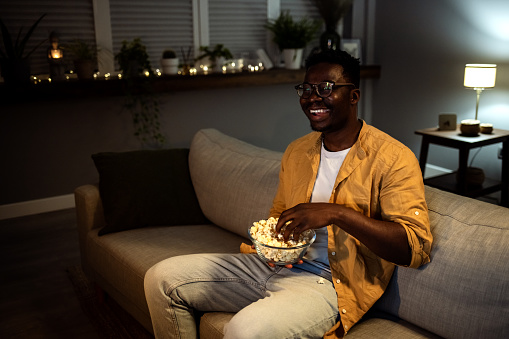 Cheerful young guy taking some popcorn from a bowl while watching comedy