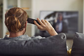 Back view portrait of modern young man watching TV at home and holding remote control, copy space