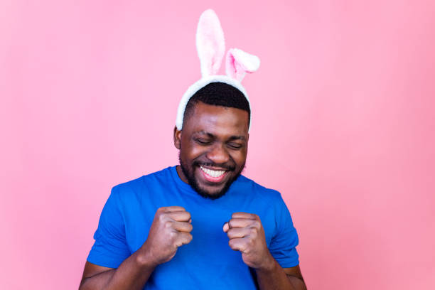 man wearing cute easter bunny ears in studio pink wall background stock photo