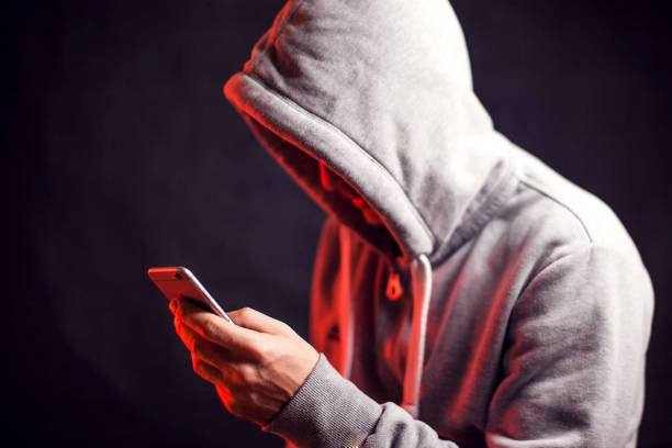 Man wearing hoody sweater with phone in hands. Crime and hacking concept Man wearing hoody sweater with mobile phone in hands. Crime and hacking concept scammer stock pictures, royalty-free photos & images