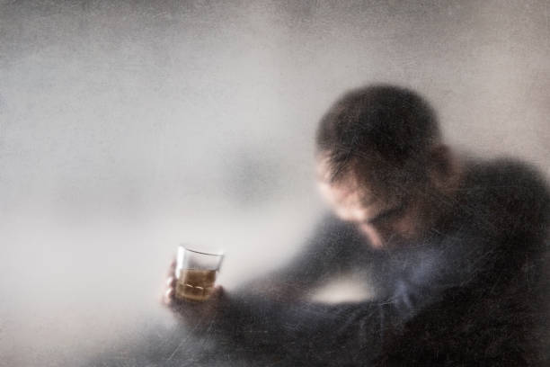 Man with a glass of whiskey behind a dusty scratched glass. Alcoholism concept. stock photo