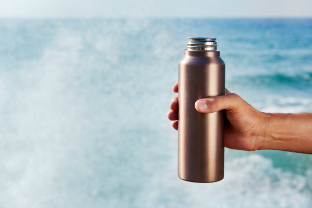 man with an aluminum reusable water bottle closeup of a man with an aluminum reusable water bottle in his hand front of the ocean reusable water bottle stock pictures, royalty-free photos & images