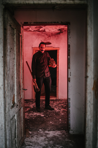 Man with an axe and a pumpkin standing in a room illuminated with red light in a rustic house