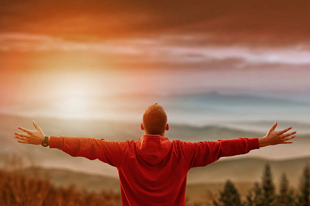 Man with arms spread looking at mountains Man with arms spread looking at mountains vivid photo with layered mountains valley in front. Man has his back facing the camera with mountains in background and sun flare effect attitude stock pictures, royalty-free photos & images