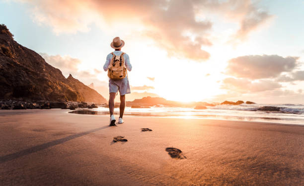 Man with backpack walking on the beach at sunset - Travel lifestyle concept - Golden filter stock photo