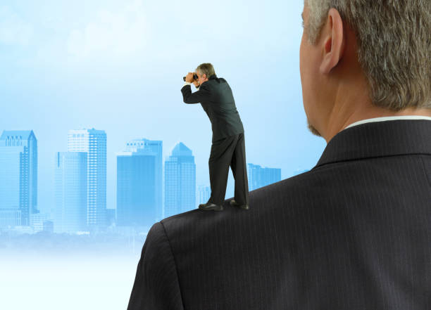 Man with binoculars looking into the distance standing on the shoulders of giants concept with cityscape background stock photo