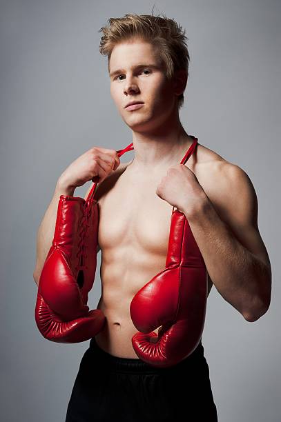 man with boxing gloves Portrait of a young blond man with boxing gloves against grey background teenage boys men blond hair muscular build stock pictures, royalty-free photos & images
