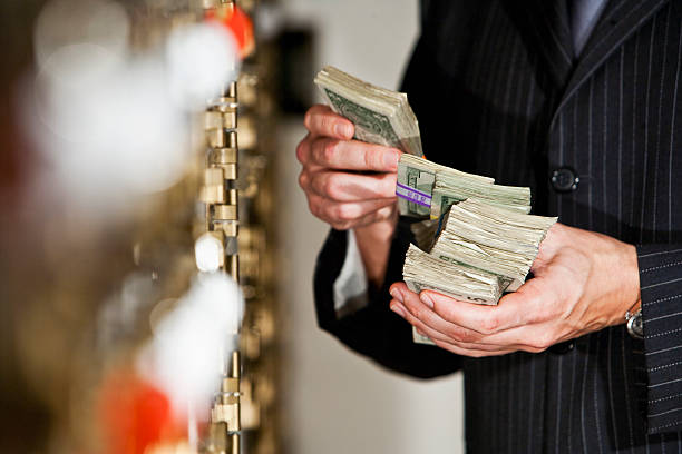 Man with cash by safety deposit boxes Man holding big stack of US paper currency by safety deposit boxes.  Focus on money money laundering stock pictures, royalty-free photos & images