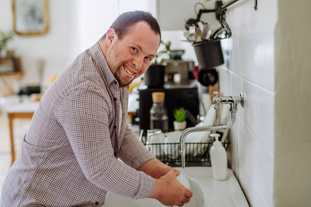 Man with down syndrome washing the dishes, taking care of himself, concept of independent and social inclusion. stock photo