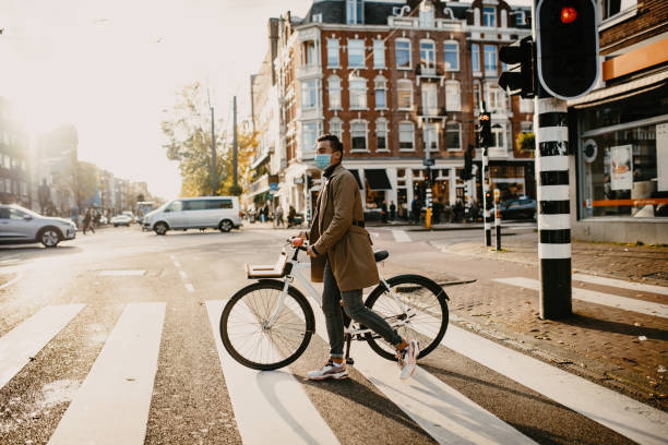 man med ansiktsmask trycka cykel i staden under coronavirus pandemi låsning - nederländerna bildbanksfoton och bilder