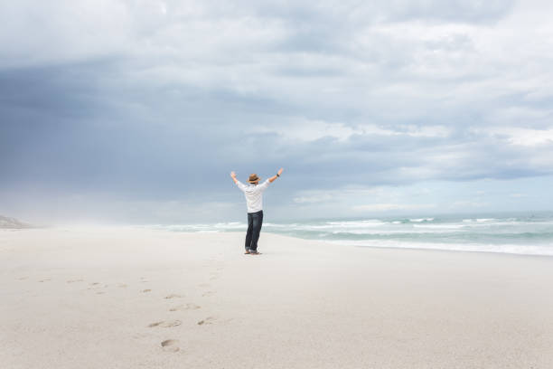 Man with hands in the air celebrating freedom on beach stock photo