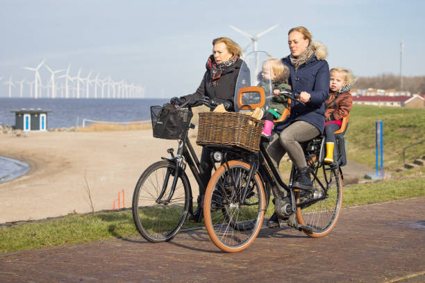 Man with his little son at bycycle near Dutch coast Urk, The Netherlands - February 19 2021: Women with little kids at bycycle near Dutch coast of Urk, in the background a view at a big wind turbine farm flevoland stock pictures, royalty-free photos & images