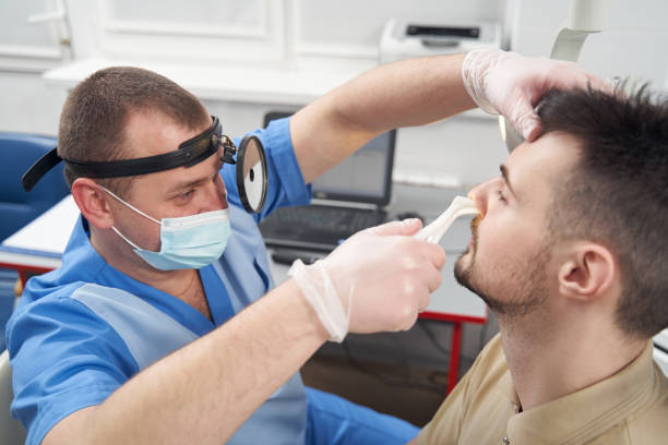 Man with runny nose visiting otorhinolaryngologist office Top view of male doctor wearing head light and using medical tongs for examining patient nosetrills physical therapy programs stock pictures, royalty-free photos & images