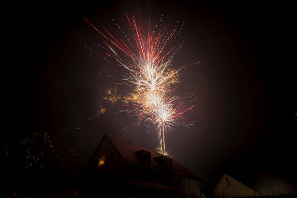 Man with sparkler in the window of a residential house watching the fireworks lightening the night sky at New Year stock photo