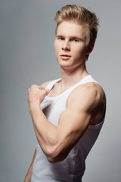 man with white t-shirt Portrait of young handsome blond man wearing t-shirt against grey background teenage boys men blond hair muscular build stock pictures, royalty-free photos & images