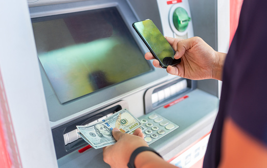 Man Withdraw Money With Smartphone At ATM.Cash Dispenser And Money Stock Photo