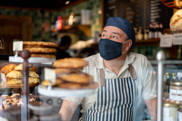 얼굴 마스크를 쓰고 커피숍에서 일하는 남자 - 빵집 뉴스 사진 이미지