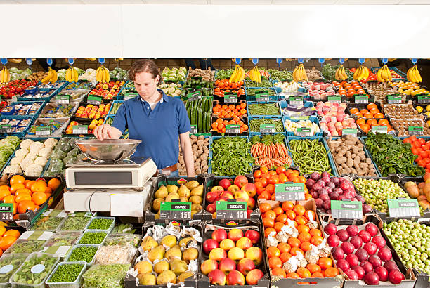 A man working at a green grocery store weighing vegetables stock photo