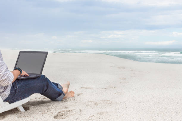Man working remotely on laptop while on the beach stock photo