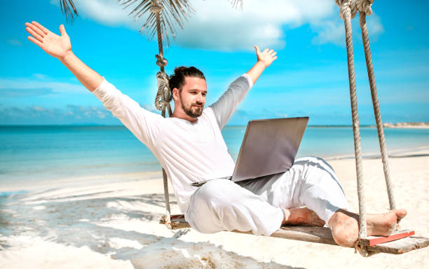 Man working with a laptop, on a hammock in the beach. Show win Man working with a laptop, on a hammock in the beach. Concept of digital nomad, remote worker, independent location entrepreneur. Show win nomadic people stock pictures, royalty-free photos & images
