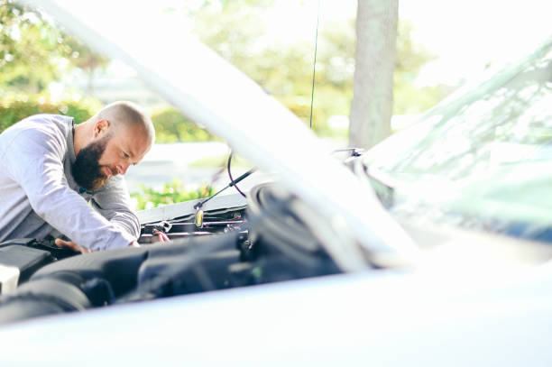 Man works on a car engine, hood up, mechanic looking under the hood stock photo