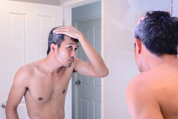 Man worried about gray hair while looking into a mirror. stock photo