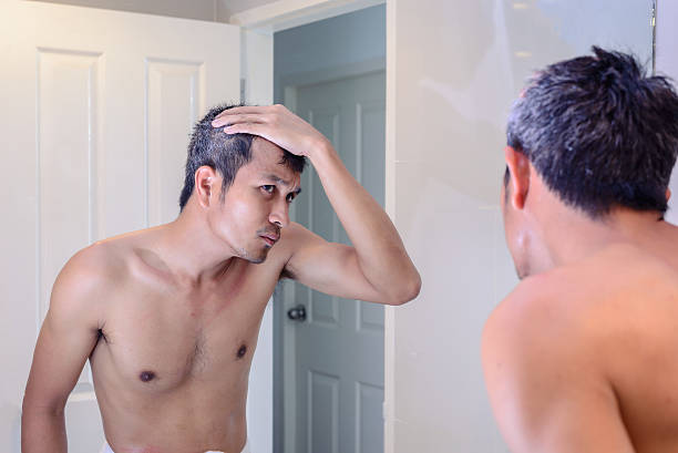Man worried about gray hair while looking into a mirror. stock photo