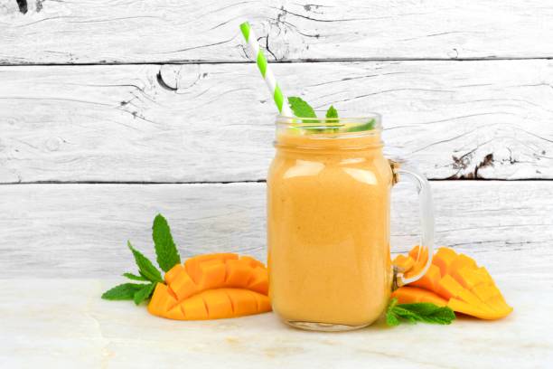 Mango coconut smoothie in a mason jar, on rustic white wood Tropical mango coconut smoothie in a mason jar glass, on a rustic white wood background mango smoothie stock pictures, royalty-free photos & images