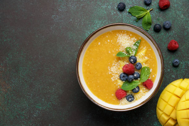 Mango smoothie bowl with coconut, raspberries and blueberries on dark background Healthy breakfast mango smoothie stock pictures, royalty-free photos & images