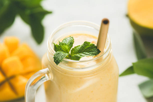 Mango smoothie in a glass Mango smoothie in a glass with bamboo drinking straw and mint leaf. Closeup view. Vegan tropical smoothie papaya smoothie stock pictures, royalty-free photos & images