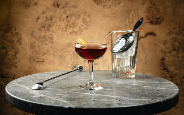 Manhattan cocktail with bar spoon and stirring glass A Manhattan or Rob Roy cocktail in a coupe glass on a round stone table. manhattan cocktail stock pictures, royalty-free photos & images