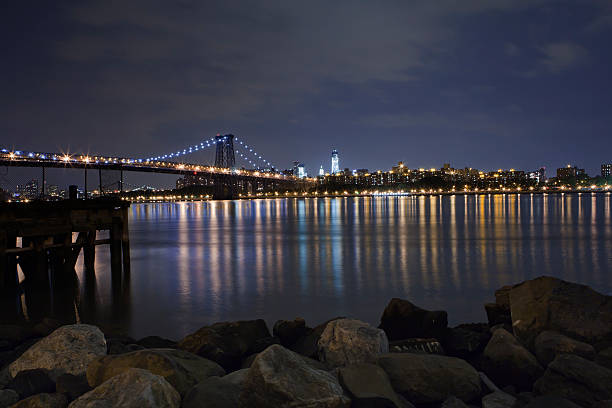 Manhattan Skyline with Williamsburg Bridge Nighttime view of the Lower East Side with the Williamsburg Bridge over the East River and World Trade Center in the Background. The Foreground shows an old dock and large rocks on the Brooklyn riverside of Grand Ferry Park. williamsburg virginia stock pictures, royalty-free photos & images