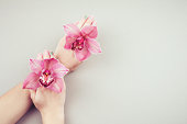 Pink tone pastel manicure hands holding two beautiful orchid flowers. Stylish manicure top view.