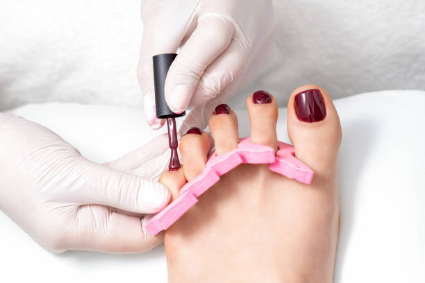 Manicure master is painting female toenails Manicure master is painting on female toenails with maroon nail polish by brush wearing white gloves pedicure stock pictures, royalty-free photos & images