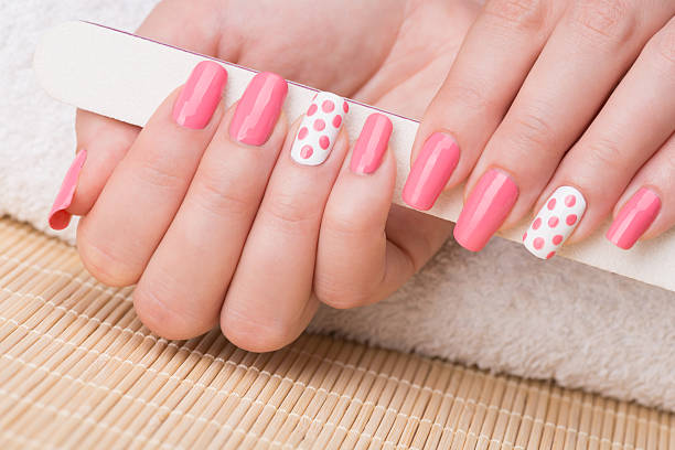Manicure Beauty treatment photo of nice manicured woman fingernails holding nail file. Feminine nail art with nice pink and white nail polish. nail salon stock pictures, royalty-free photos & images