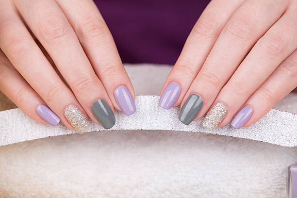 Manicure Beauty treatment photo of nice manicured woman fingernails holding a nail file. Very nice feminine nail art with nice purple,silver and grayish nail polish. artificial nail stock pictures, royalty-free photos & images