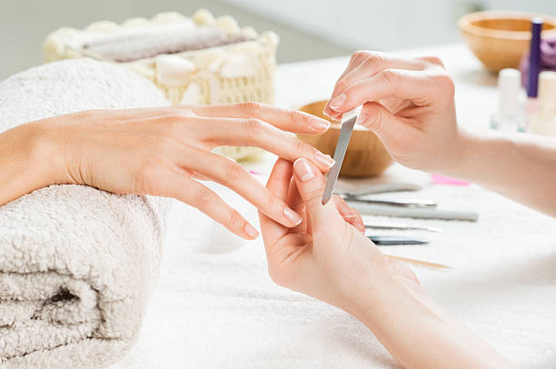 Manicure treatment at nail salon Closeup shot of a woman in a nail salon receiving a manicure by a beautician with nail file. Woman getting nail manicure. Beautician file nails to a customer. Shallow depth of field with focus on nailfile. nail file stock pictures, royalty-free photos & images