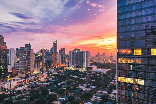 Downtown Manila view over Makati District under colorful sunset light.  Aerial view towards the Makati Skyscrapers. Partly illuminated modern skyscraper in the foreground. Makati, Manila, Philippines, Southeast Asia, Asia
