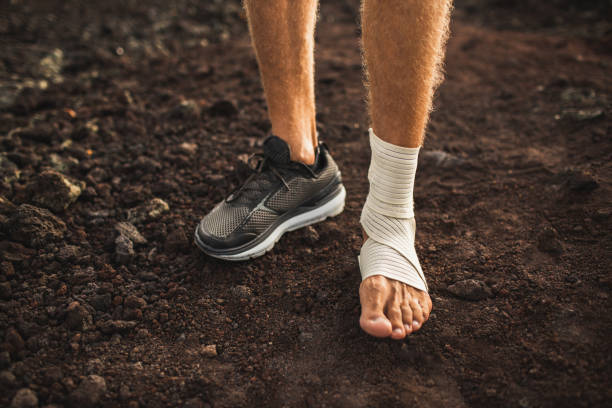 Man's ankle in compression bandage. Leg injury while trail running outdoors.  First aid for sprained ligament or tendon. stock photo